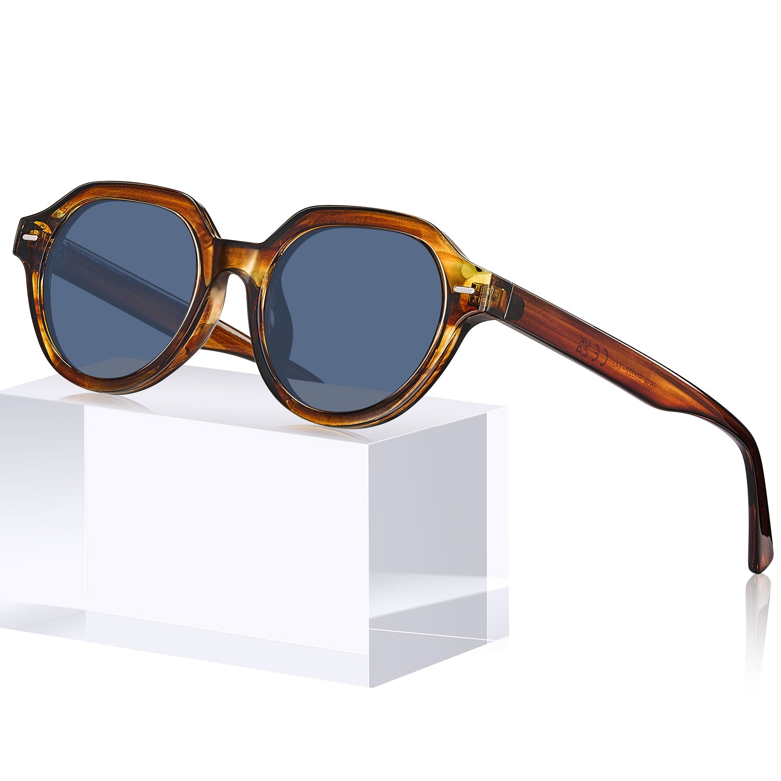 Oversized round sunglasses with a translucent tortoiseshell frame and dark blue-gray lenses, displayed on a white geometric pedestal against a white background.