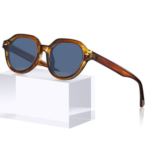 Oversized round sunglasses with a translucent tortoiseshell frame and dark blue-gray lenses, displayed on a white geometric pedestal against a white background.