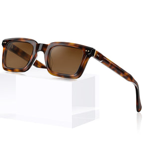 Square sunglasses with a brown tortoiseshell frame and brown tinted lenses, displayed on a white block against a white background.